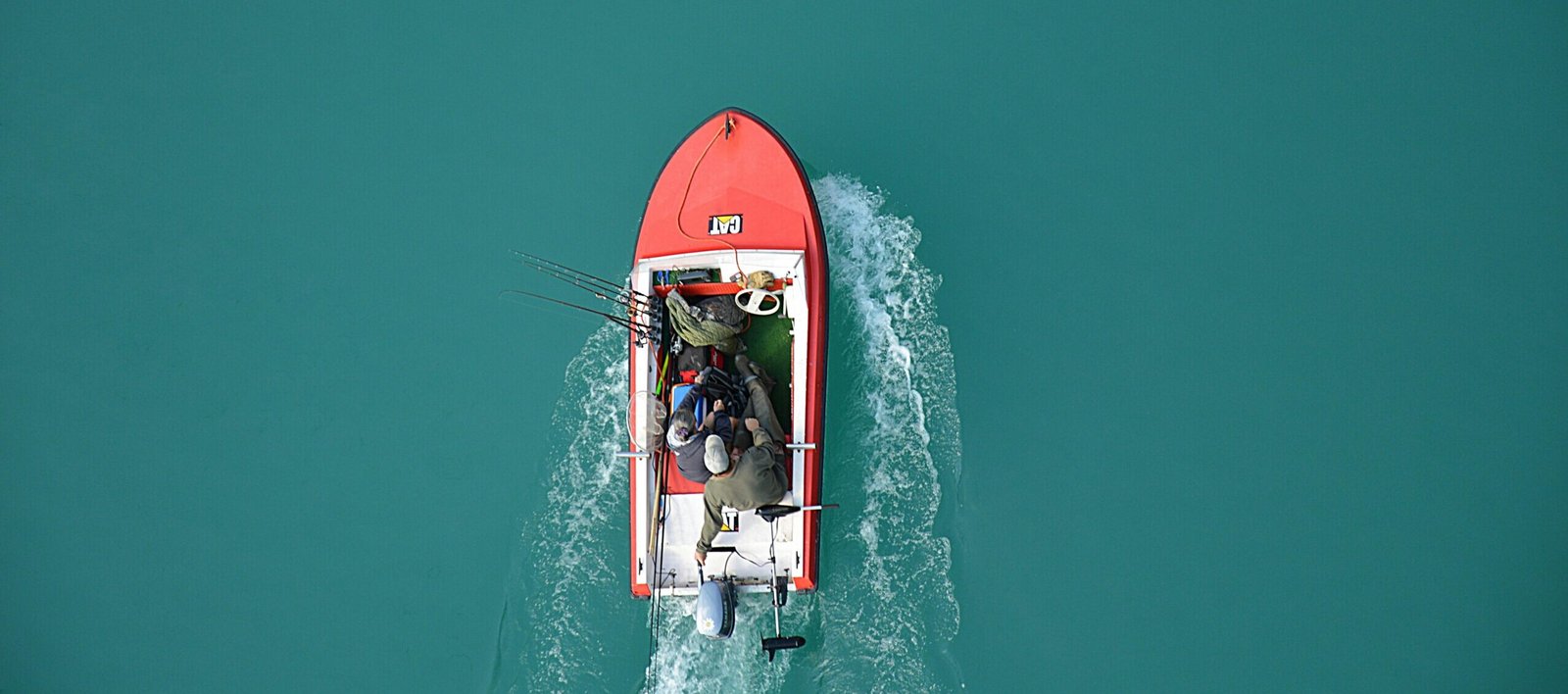 Top view of a red motorboat with fishermen navigating open turquoise waters.
